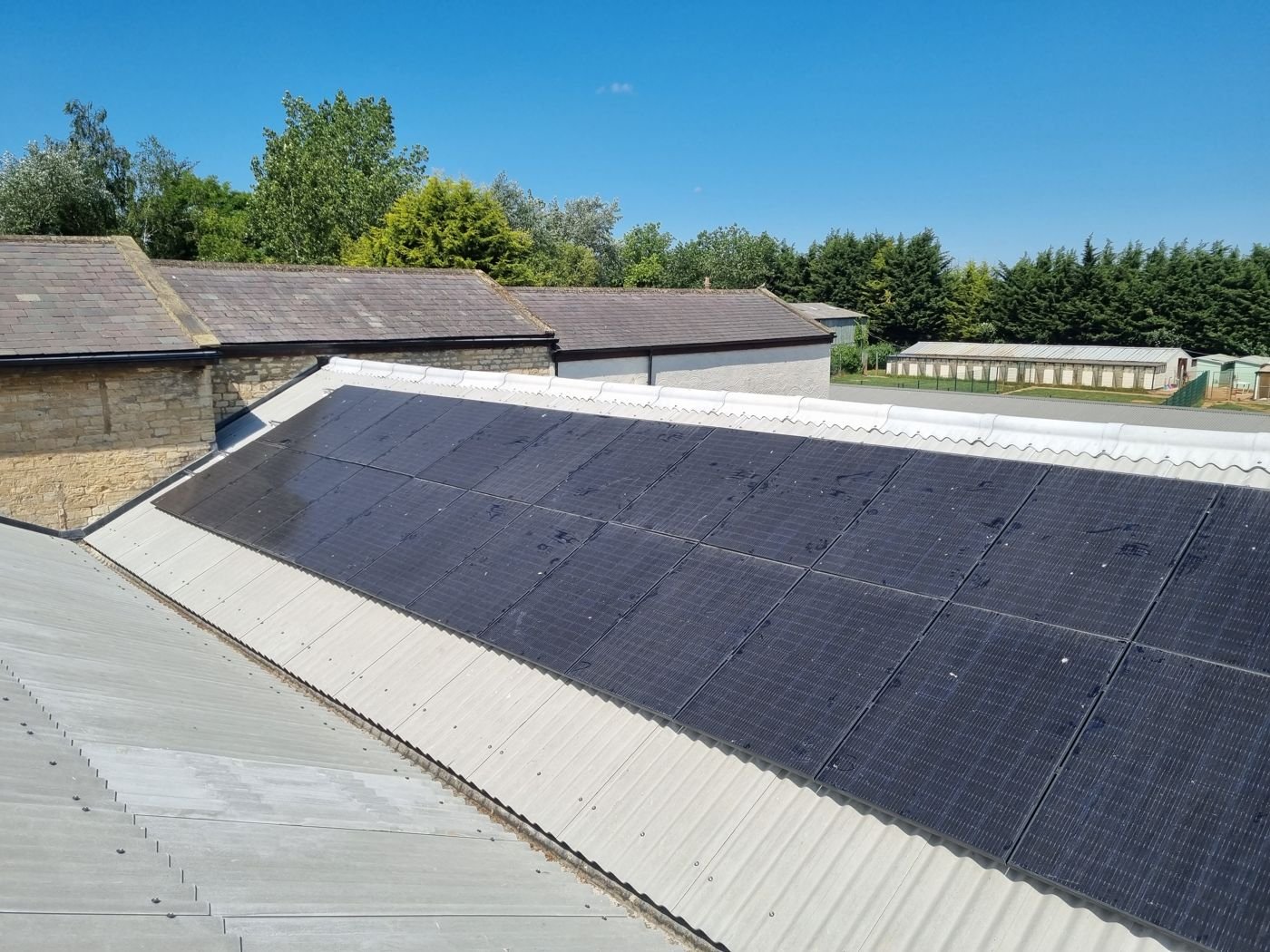 All-black solar panels on the corrugated sheet roof of a farm building on a sunny day