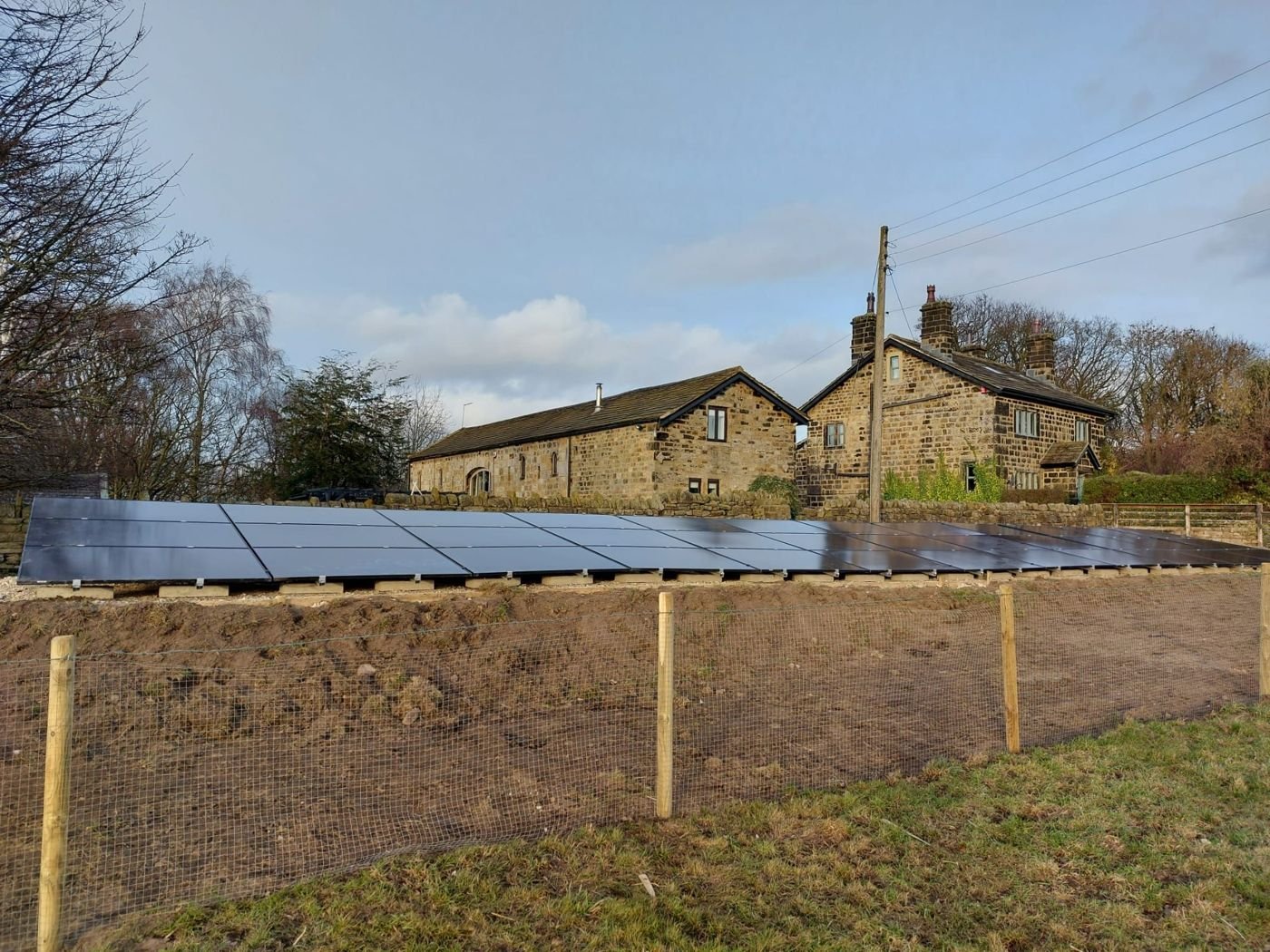 A fenced ground-mounted solar array in front of stone farmhouses