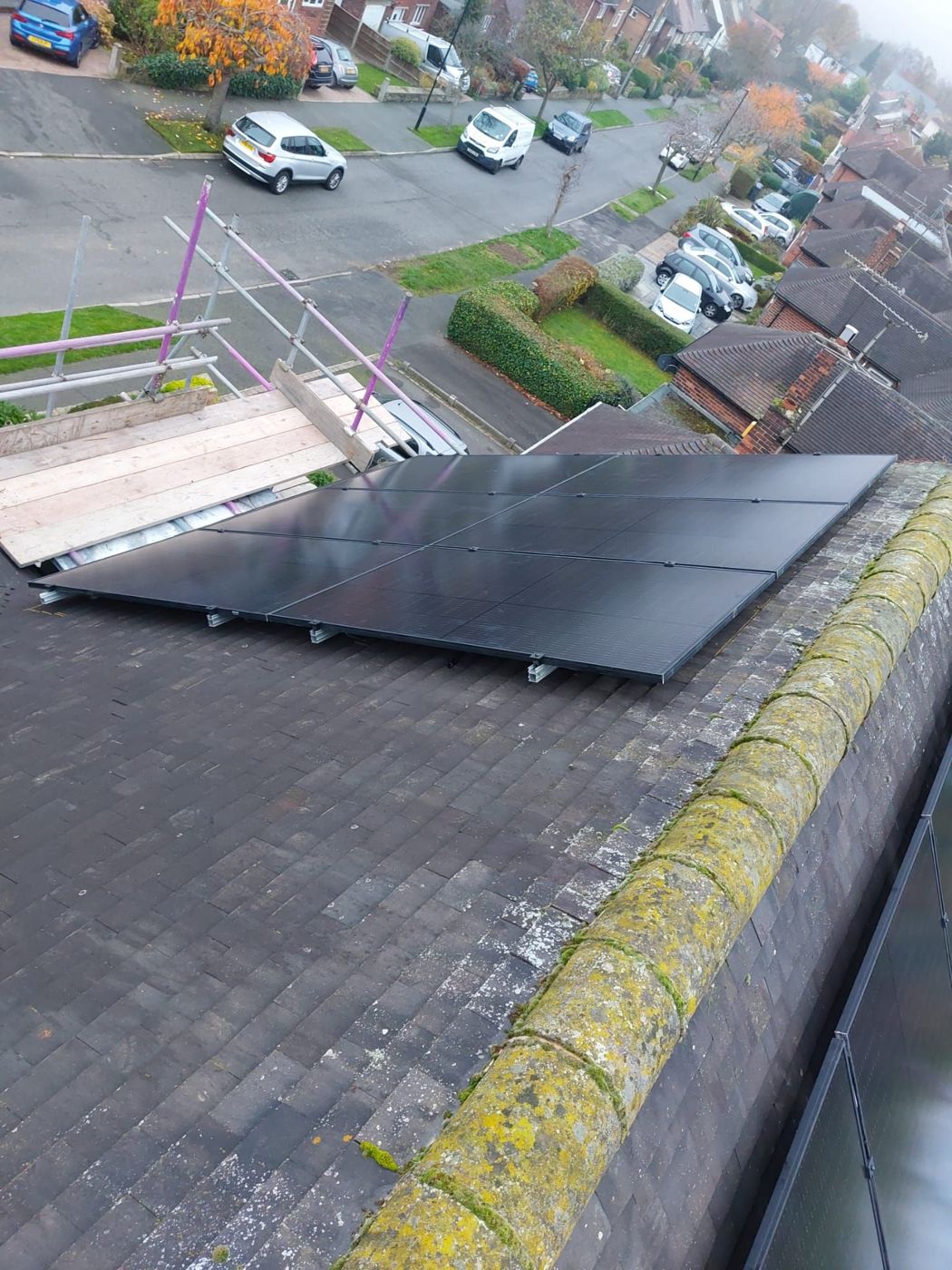 All-black solar panels on a dark slate-style tile roof above a suburban street