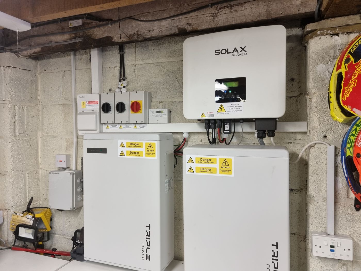 A SolaX hybrid inverter with two Triple Power batteries on a garage wall