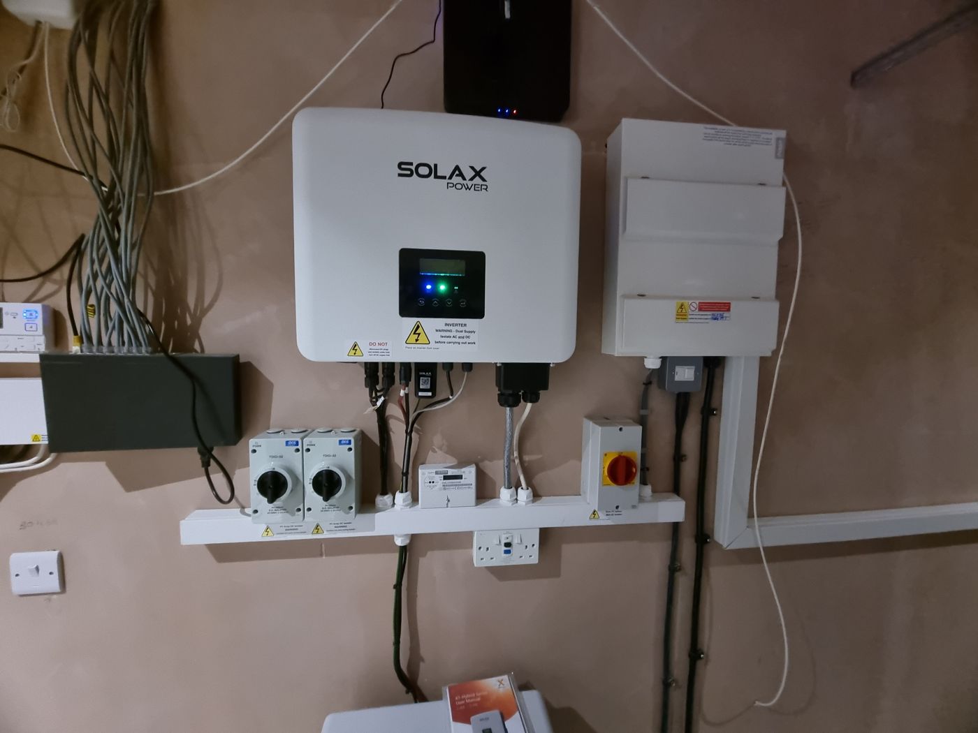 A SolaX inverter on a wall with DC and AC isolator switches and a consumer unit, with no battery