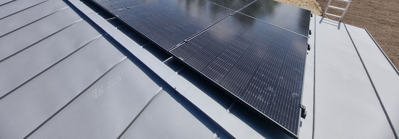 All-black solar panels clamped to the raised seams of a grey standing-seam metal roof