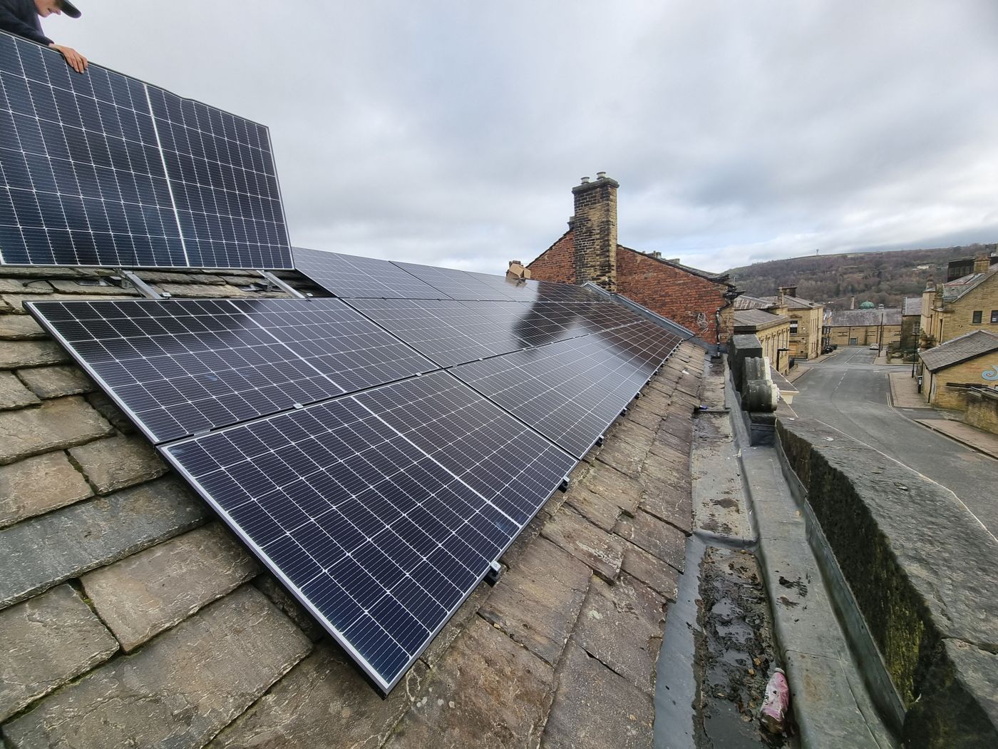 Blue mono solar panels on a stone-slate terrace roof above a hilly town street